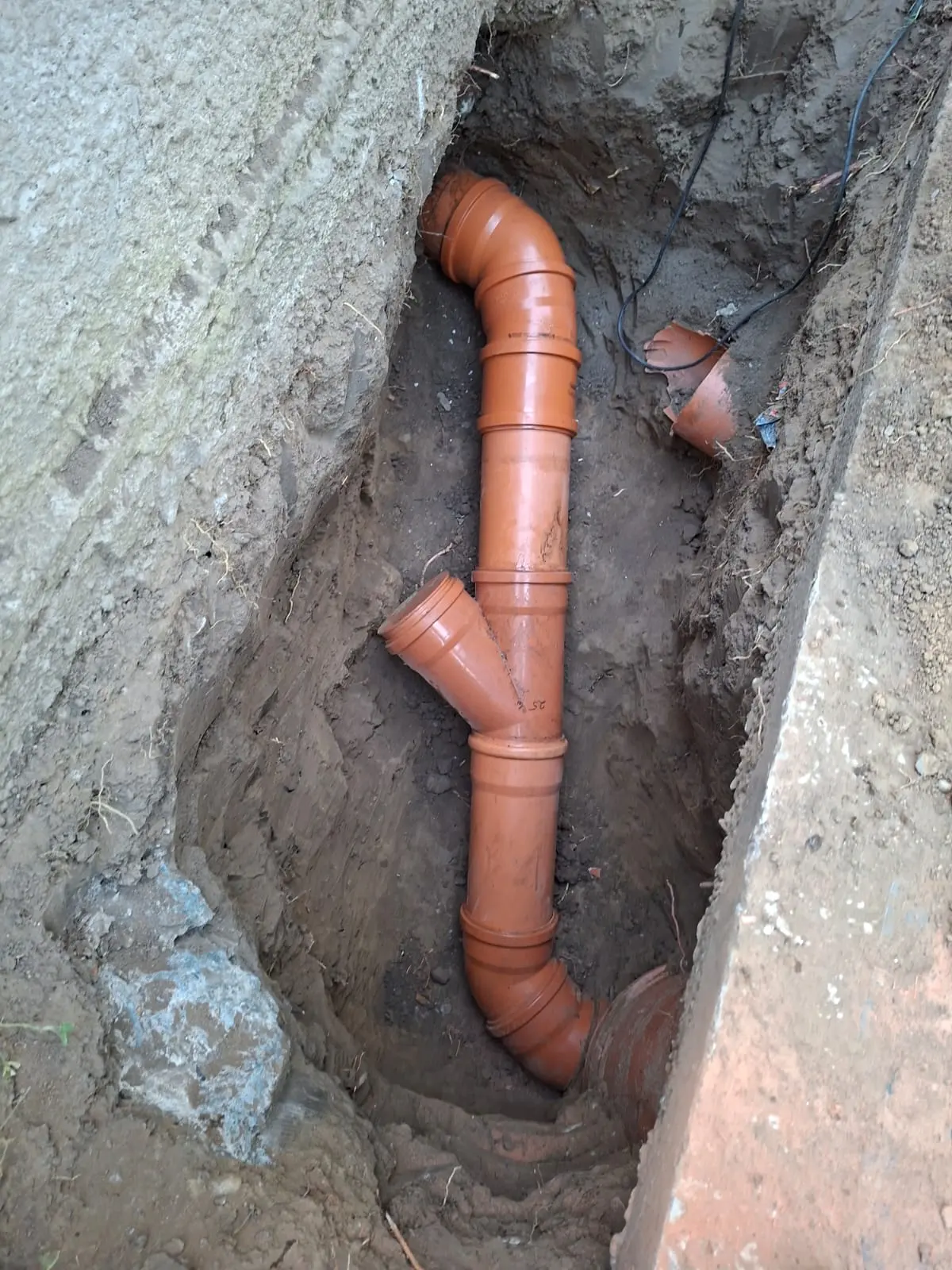 Tub de canalizare PVC cu coturi și ramificație, poziționat pe traseu în tranșee.