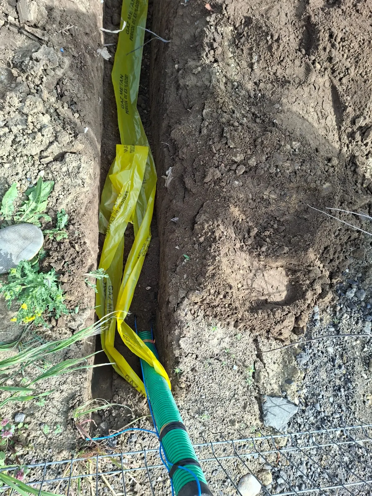 Traseu de gaz în tranșee, cu banda galbenă de semnalizare și conducta verde dedesubt.